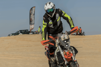 Pilote de moto cross en action sur une piste de sable, casque tout-terrain blanc et masque, lors d'une course en plein air